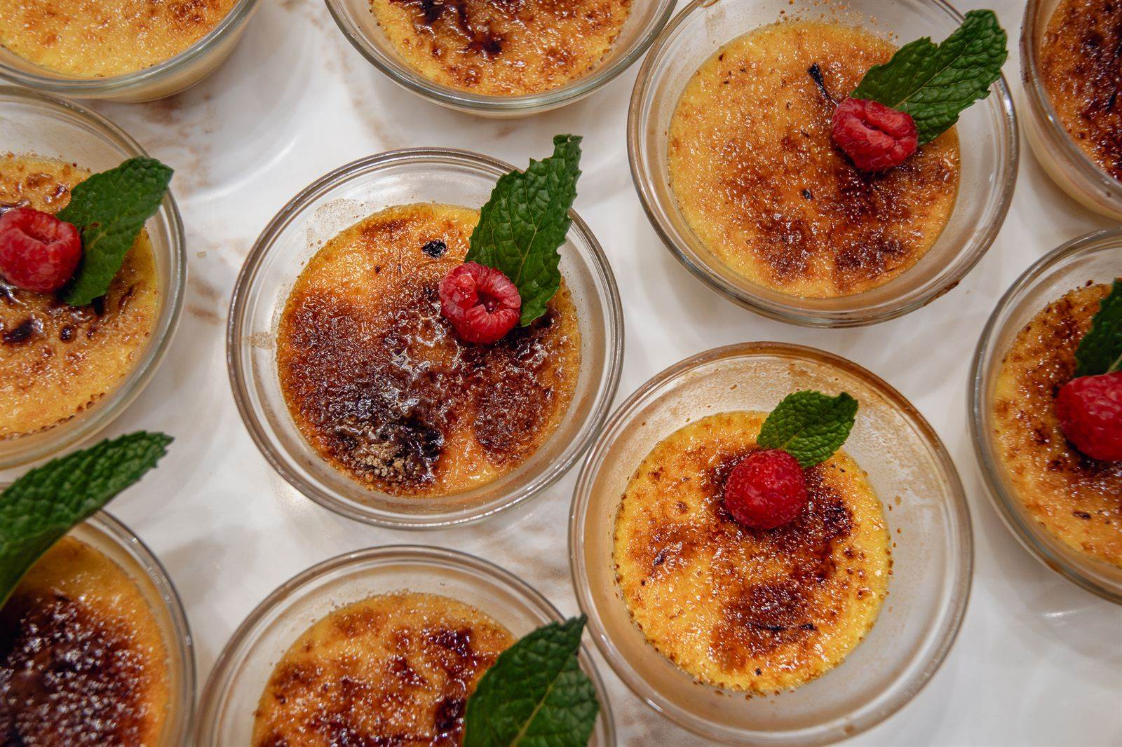 Rows of crème brûlée topped with raspberries and mint