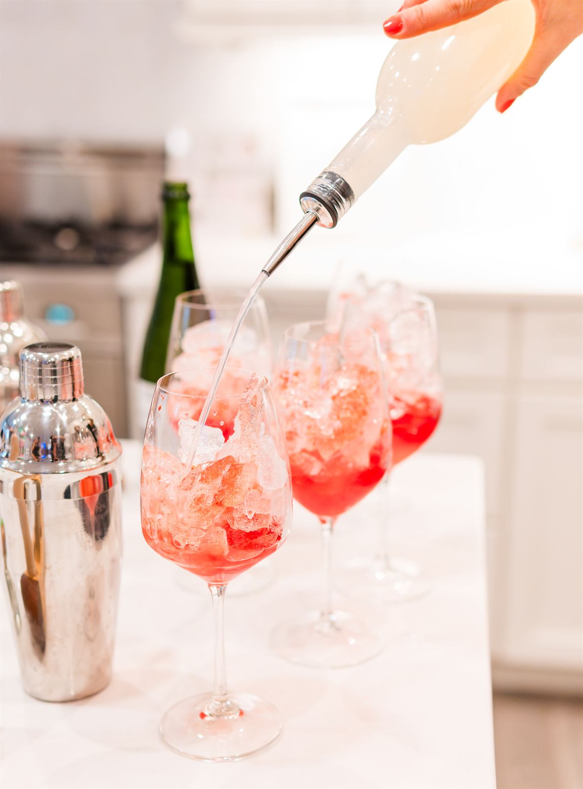 Pink cocktails being poured over ice next to a cocktail shaker