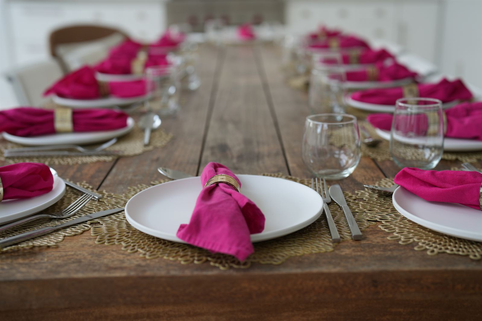 Long wooden table set with white plates and hot-pink napkins