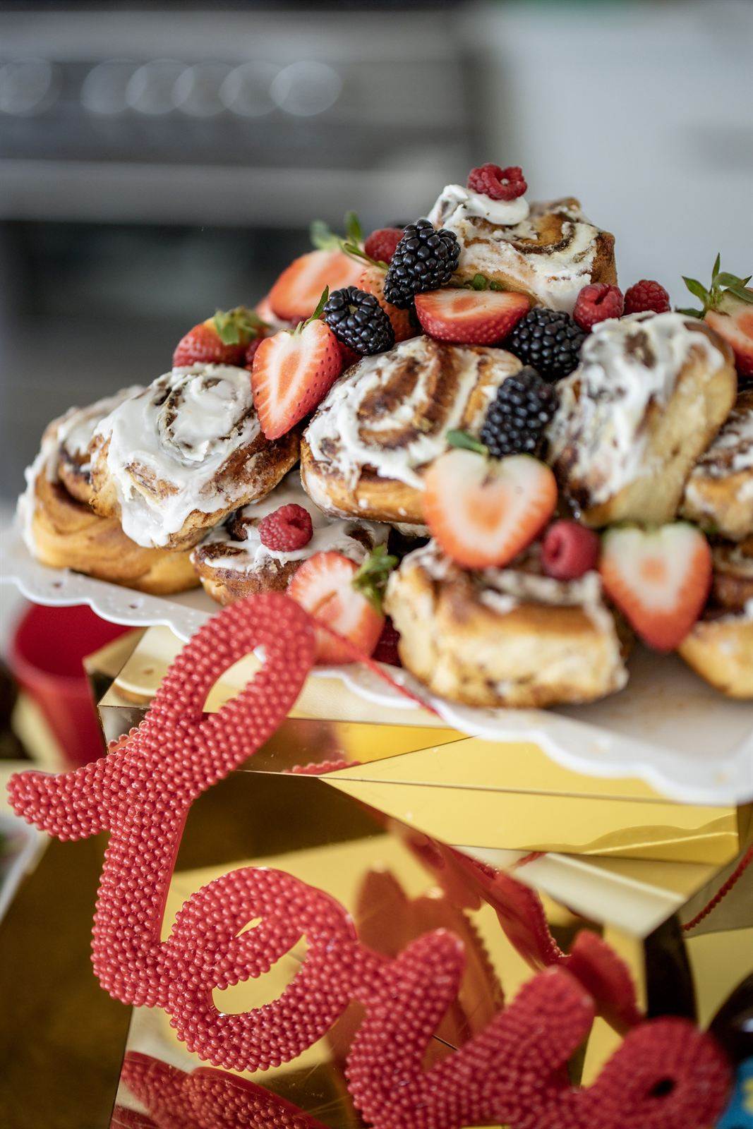 Cinnamon rolls topped with strawberries and blackberries beside a red love sign