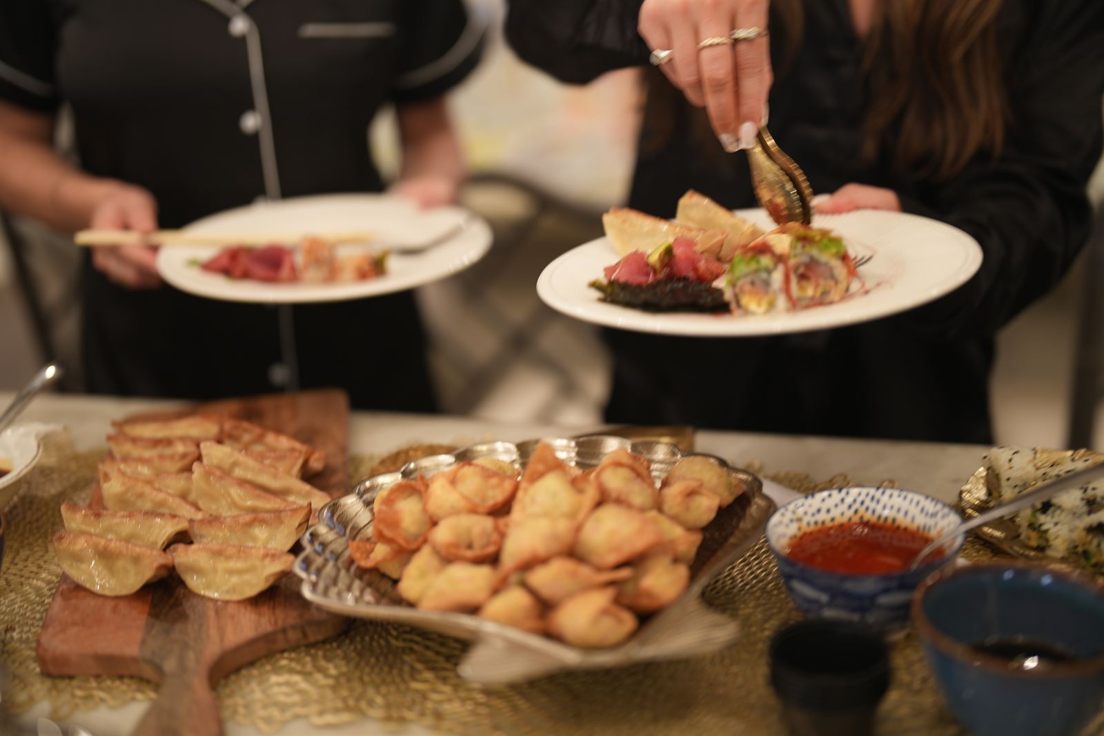 Bachelorette guests helping themselves to sushi rolls and wontons at a kitchen island