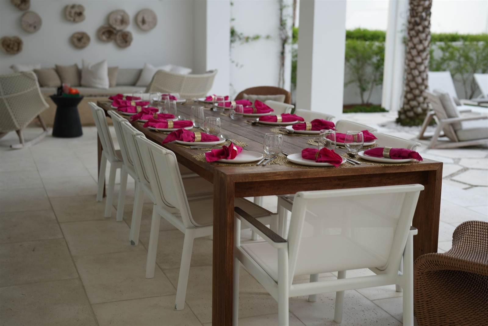Long outdoor dining table set with white plates, wine glasses and hot-pink napkins