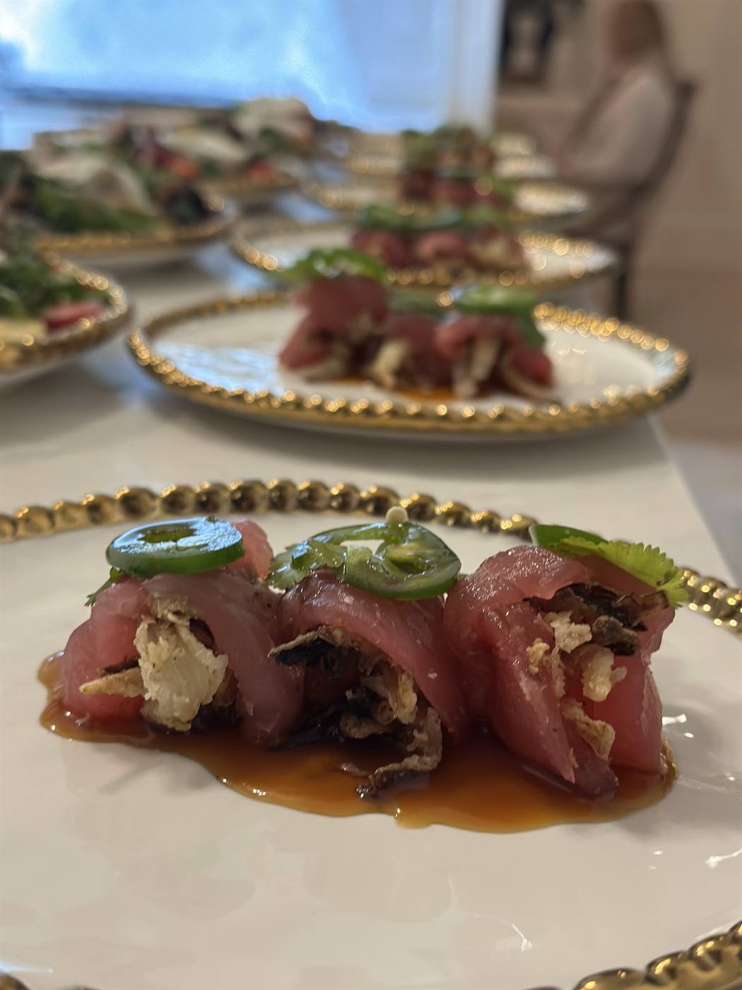 Ahi tuna crudo topped with sliced jalapeño on gold-rimmed plates