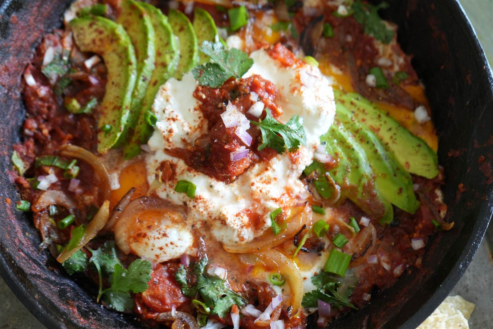 Shakshuka with poached eggs and sliced avocado in a cast-iron skillet